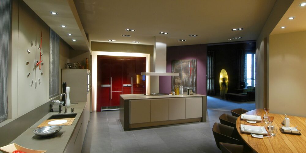 Cocina moderna y contemporánea de alta gama en Barcelona con cabinetry elegante en tonos neutros, materiales de alta calidad como mármol y madera, y una gran mesa de comedor de madera. El espacio combina funcionalidad y estética con iluminación natural y diseño minimalista.