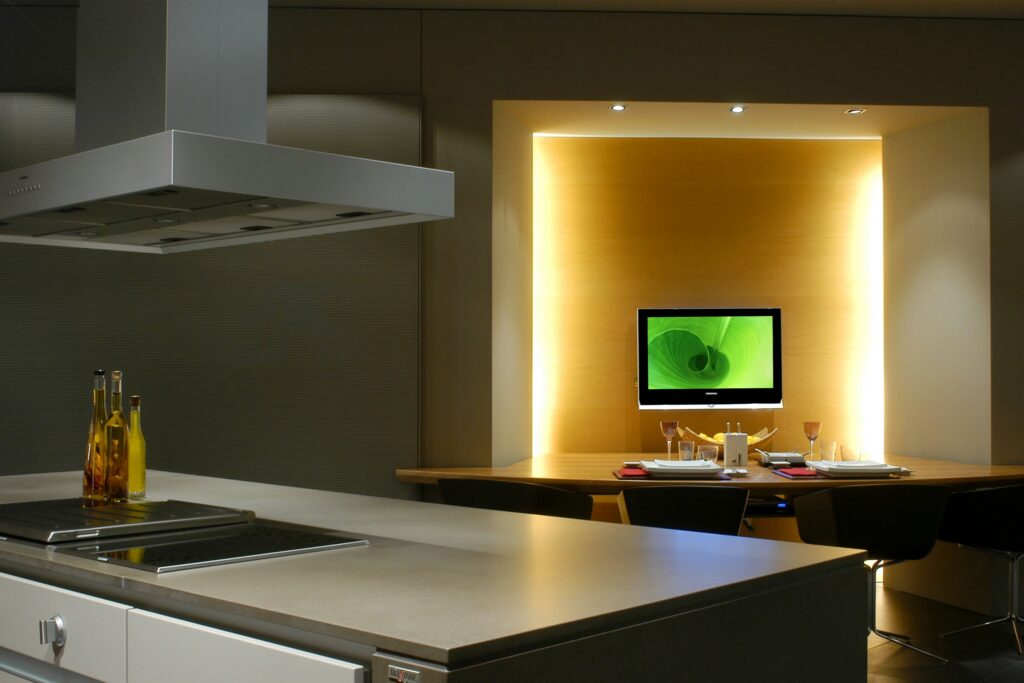Cocinas en Casa Decor: Una cocina contemporánea que presenta un diseño minimalista con una isla de acero inoxidable, cocina integrada y un elegante comedor iluminado por luz ambiental.