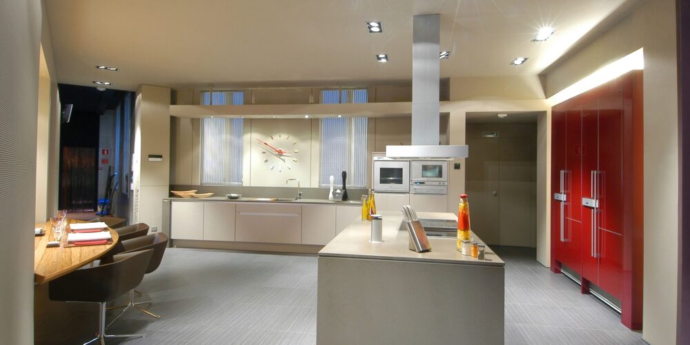 Una cocina contemporánea que muestra una estética elegante y minimalista con una isla central gris, electrodomésticos empotrados y llamativos refrigeradores rojos contra muebles de tonos neutros.