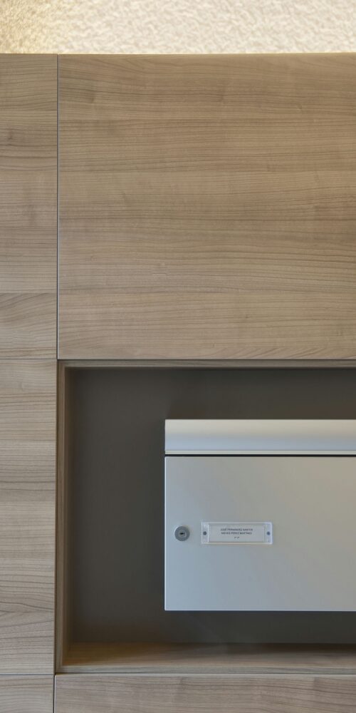 Unidad de pared de madera minimalista con buzón integrado en un espacio contemporáneo de alta gama en Barcelona, destacando materiales de alta calidad y un diseño sofisticado.