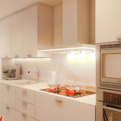 Moderna cocina de diseño interior en Barcelona, armarios blancos, electrodomésticos de acero inoxidable, encimera con placa de cocción, iluminación natural y muebles personalizados en un entorno elegante y contemporáneo.