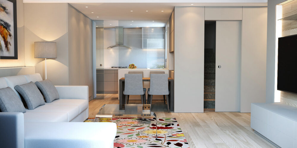 Proyecto de diseño de interiores contemporáneo en Barcelona con una amplia sala de estar que incluye un sofá blanco, alfombra colorida y mesa de café, además de un comedor adyacente con sillas elegantes y cocina de alta gama en madera y mármol, iluminado naturalmente.