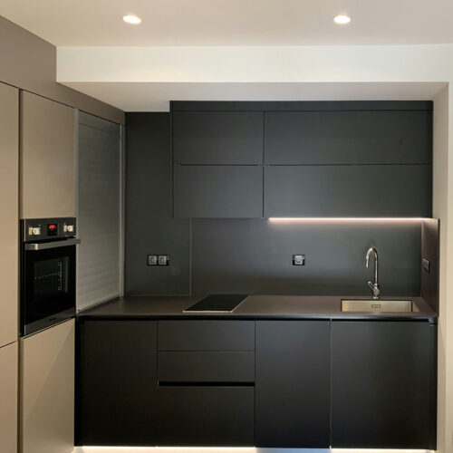 Cocina contemporánea con acabados de lujo y diseño minimalista en Barcelona. Muebles oscuros con superficies lisas, electrodomésticos integrados, encimera aerodinámica con fregadero y estufa incorporados, y luces LED sutiles que destacan su estética.