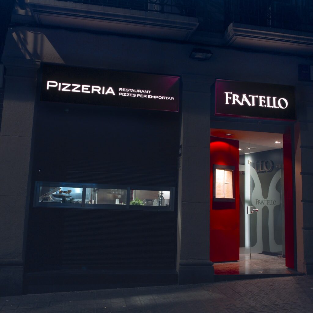 Encantadora Vista Nocturna de Fratello Pizzeria con Doble Cartelera Vista exterior de Fratello Pizzeria por la noche con señalización vibrante para pizzas para llevar y una entrada elegante, creando una atmósfera de comedor acogedora.