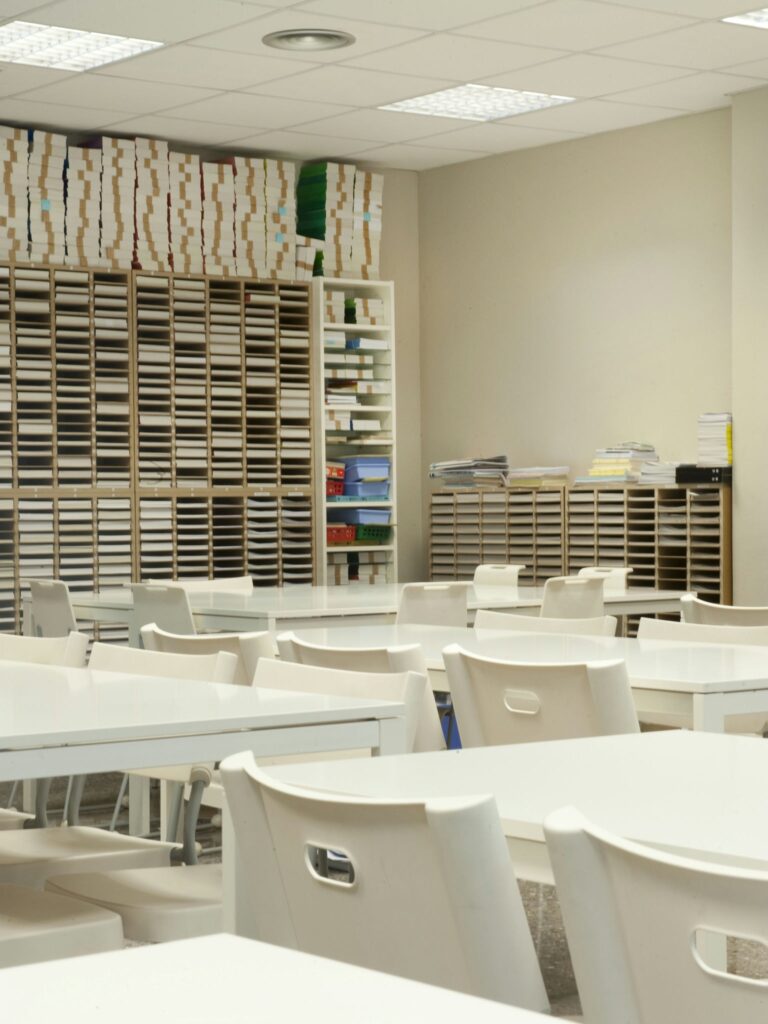 Aula Brillante y Espaciosa para un Aprendizaje Efectivo Una aula brillante y espaciosa con mesas y sillas blancas, estantes organizados con diversos materiales y paredes suaves en tonos neutros, creando un ambiente de aprendizaje ideal.