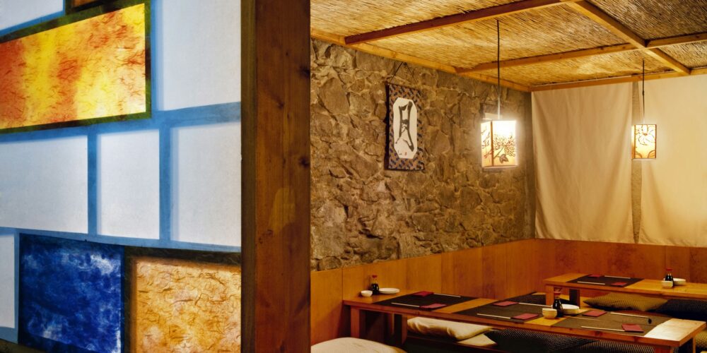 Diseño de interiores de un restaurante moderno en Barcelona con paneles coloridos en tonos amarillos y azules, asientos bajos en un ambiente cálido y acogedor, y elementos de arquitectura contemporánea.