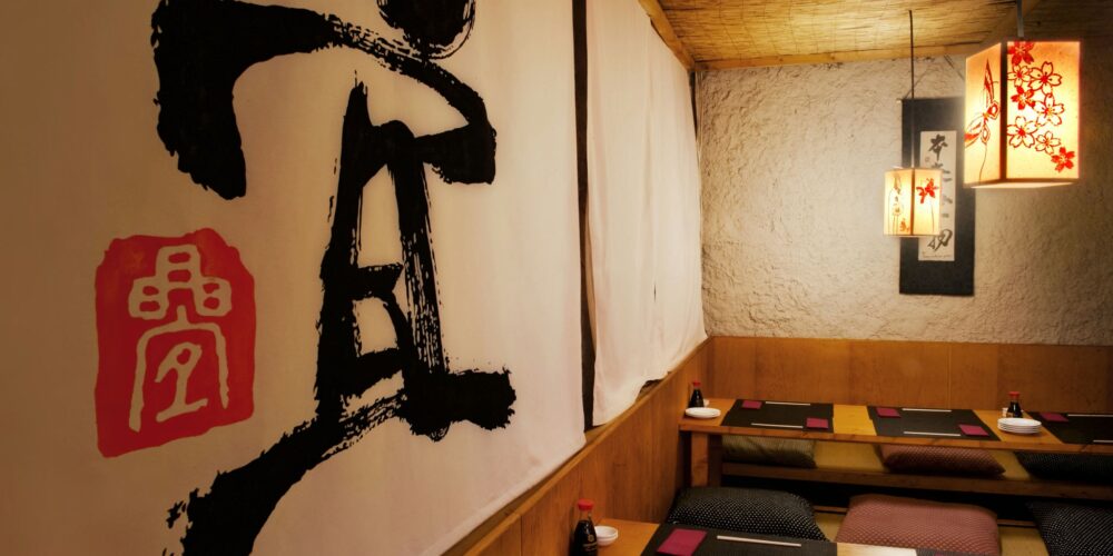 Interior elegante de un restaurante en Barcelona, con paredes de madera texturizada, arte en caligrafía japonesa y iluminación suave de faroles de papel, ideal para cenas íntimas.