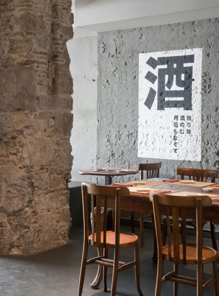 Diseño Interior de Comedor Moderno en Barcelona Comedor moderno en Barcelona con paredes de piedra rústica y una mesa de madera elegante con sillas, decorado con una obra de arte en blanco y negro. El espacio destaca la luz natural y detalles arquitectónicos sofisticados, fusionando funcionalidad y estética.