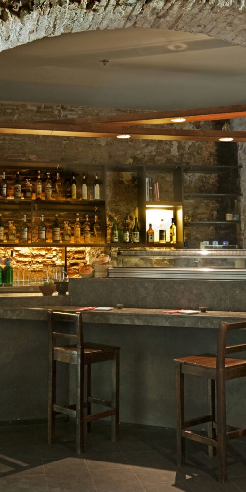 Interior de un bar en Barcelona con estética contemporánea, mostrando un amplio contador de mármol, taburetes de madera y paredes de ladrillo expuesto, ideal para amantes del diseño de interiores.