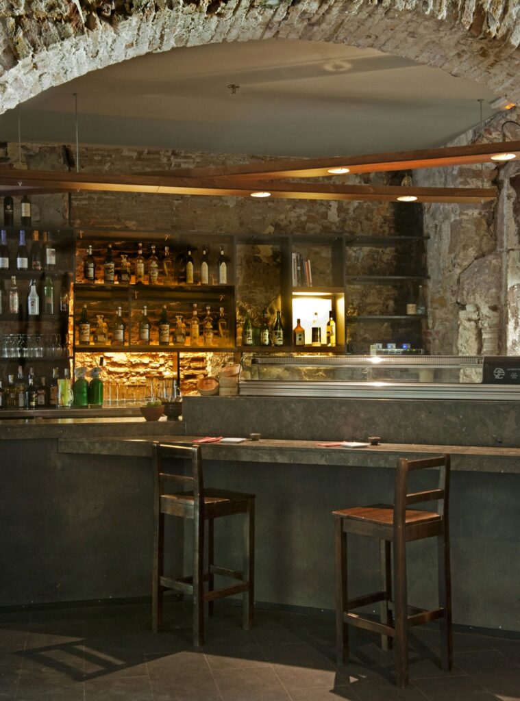 Bar moderno en Barcelona con diseño de interiores de alta gama Interior de un bar en Barcelona con estética contemporánea, mostrando un amplio contador de mármol, taburetes de madera y paredes de ladrillo expuesto, ideal para amantes del diseño de interiores.