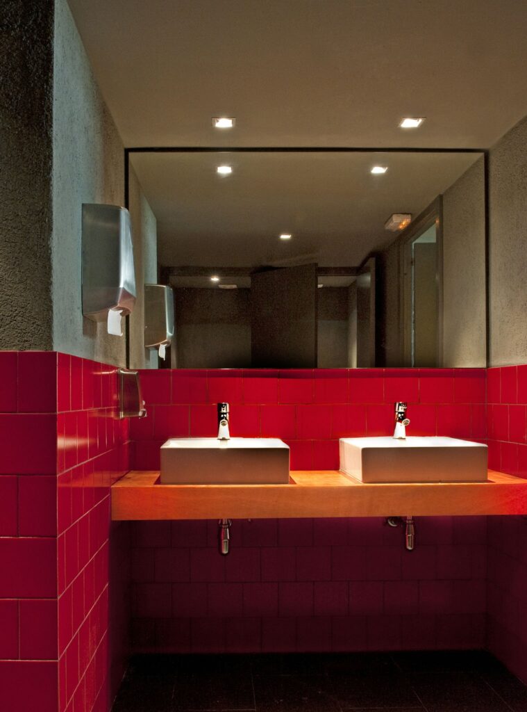 Diseño de baño moderno en Barcelona con lavabo de madera y azulejos rojos Interior moderno de un baño en Barcelona con dos lavabos rectangulares sobre una encimera de madera, azulejos rojos brillantes, accesorios de acero inoxidable y iluminación empotrada.