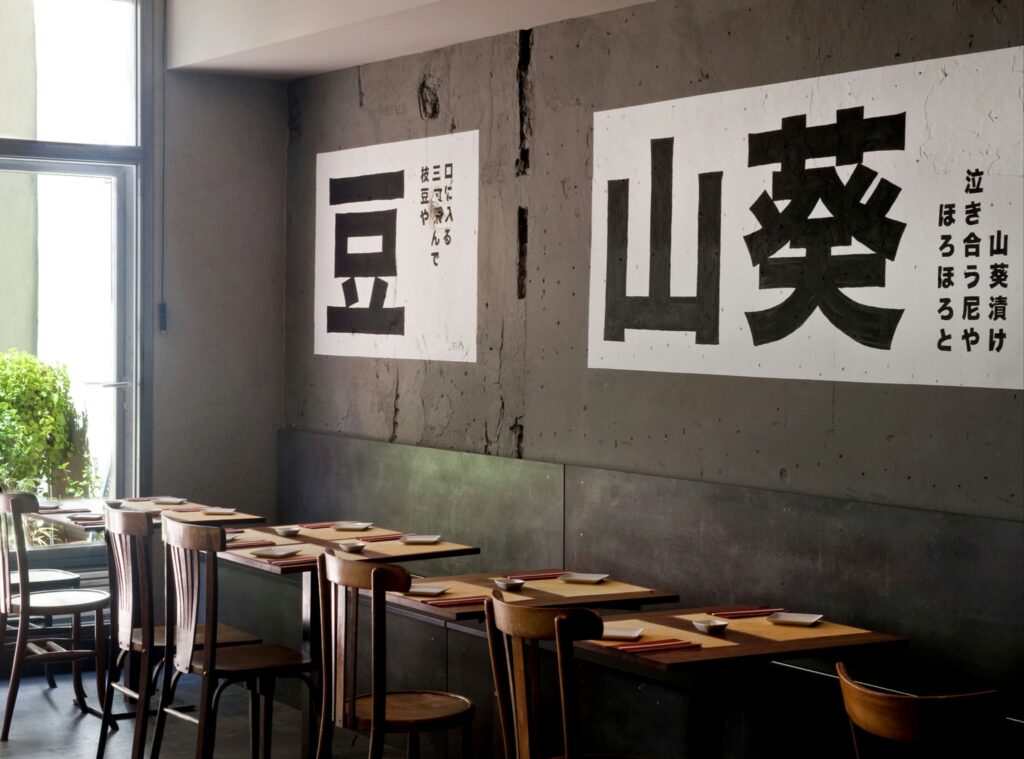 Diseño moderno de restaurante en Barcelona con elementos gráficos en blanco y negro Interior de un restaurante en Barcelona con pared de cemento, elementos gráficos en blanco y negro, mesas de madera y luz natural.