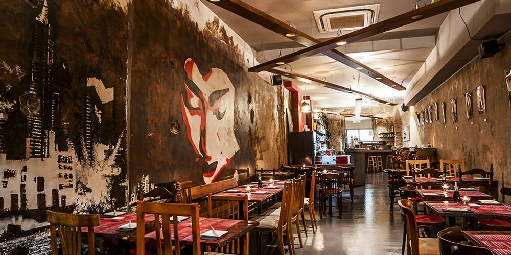 Vista interior de un restaurante contemporáneo en Barcelona, destacando un mural artístico en la pared y muebles de madera con detalles arquitectónicos elegantes.