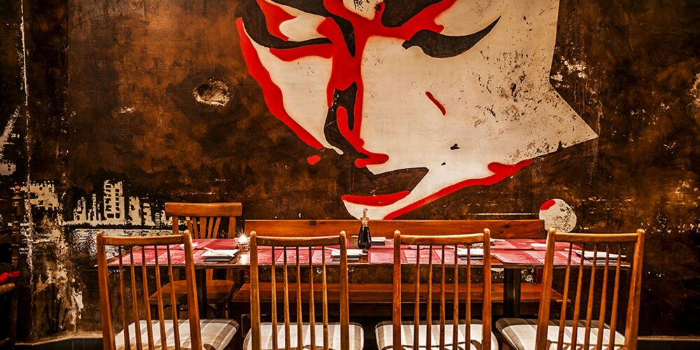 Restaurante Doble Zer00: Interiores de alta gama en Barcelona: mesa de comedor rodeada de sillas de madera, mural estilizado en la pared oscura, y decoración contemporánea.