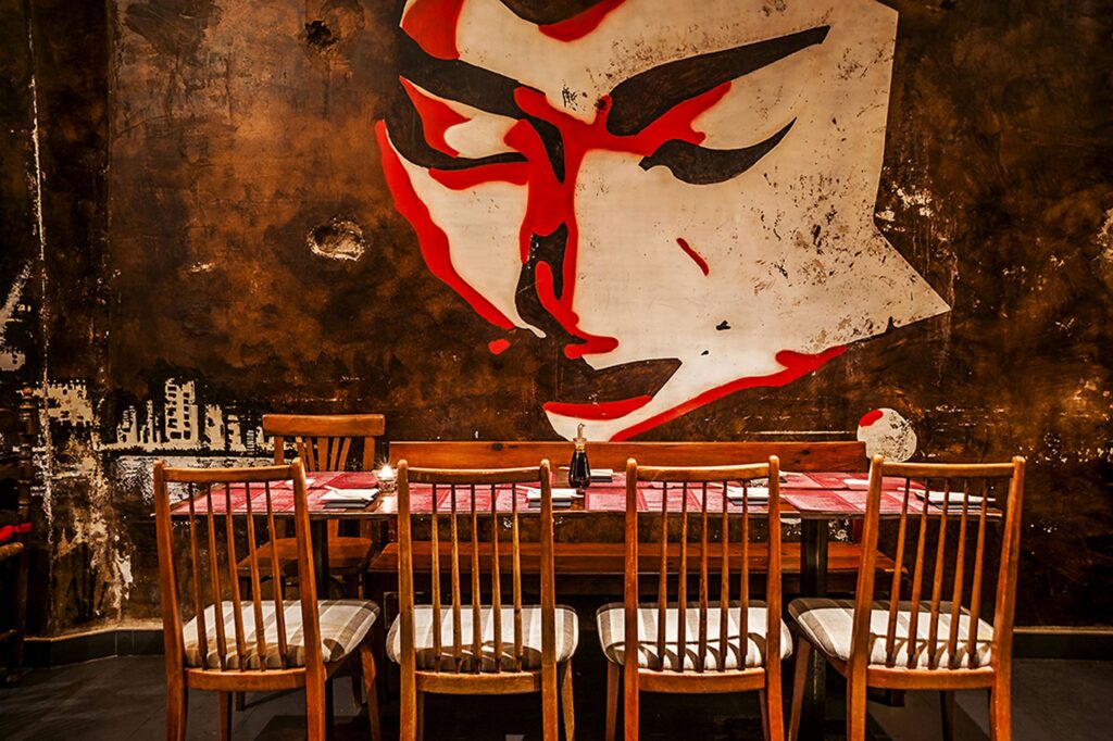 Restaurante Doble Zer00: Interiores de alta gama en Barcelona: mesa de comedor rodeada de sillas de madera, mural estilizado en la pared oscura, y decoración contemporánea.