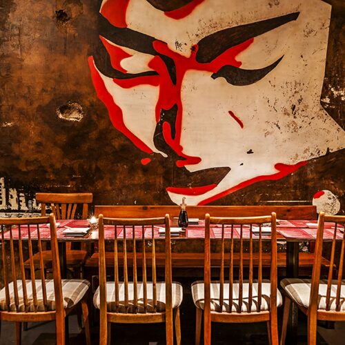 Restaurante Doble Zer00: Interiores de alta gama en Barcelona: mesa de comedor rodeada de sillas de madera, mural estilizado en la pared oscura, y decoración contemporánea.