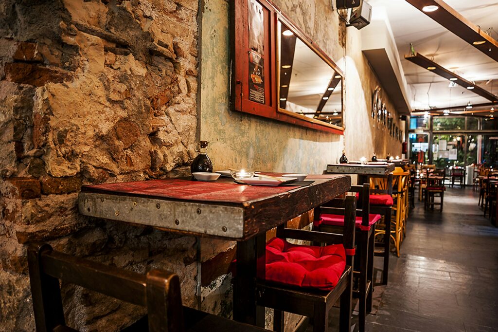 Interior moderno de un restaurante de alta gama en Barcelona con diseño elegante Vista interior de un restaurante contemporáneo en Barcelona, con paredes de piedra expuesta, mobiliario de madera y una mesa metálica con sillas rojas, destacando la funcionalidad y estética moderna.