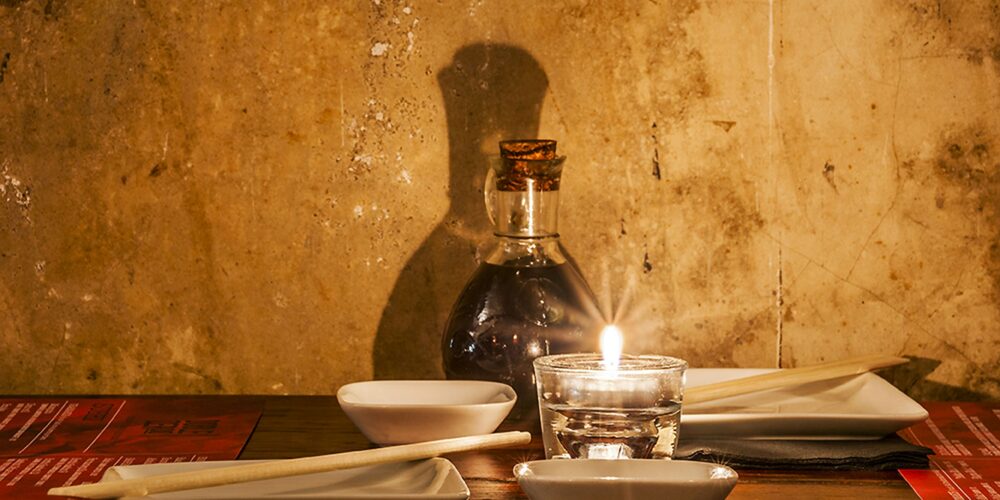 Mesa de comedor con platos blancos minimalistas, palillos elegantes y una decantadora de vidrio, ambientada con una vela suave en un entorno de diseño de interiores de alta gama en Barcelona.