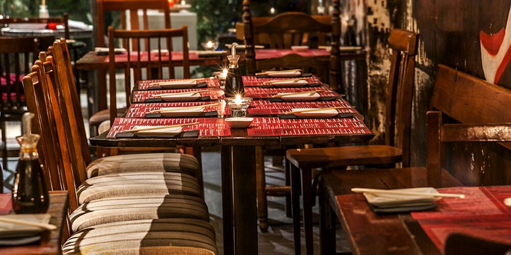 Vista interior de un restaurante contemporáneo en Barcelona, con mesas y sillas de madera, manteles rojos y velas, resaltando un diseño funcional y estético.