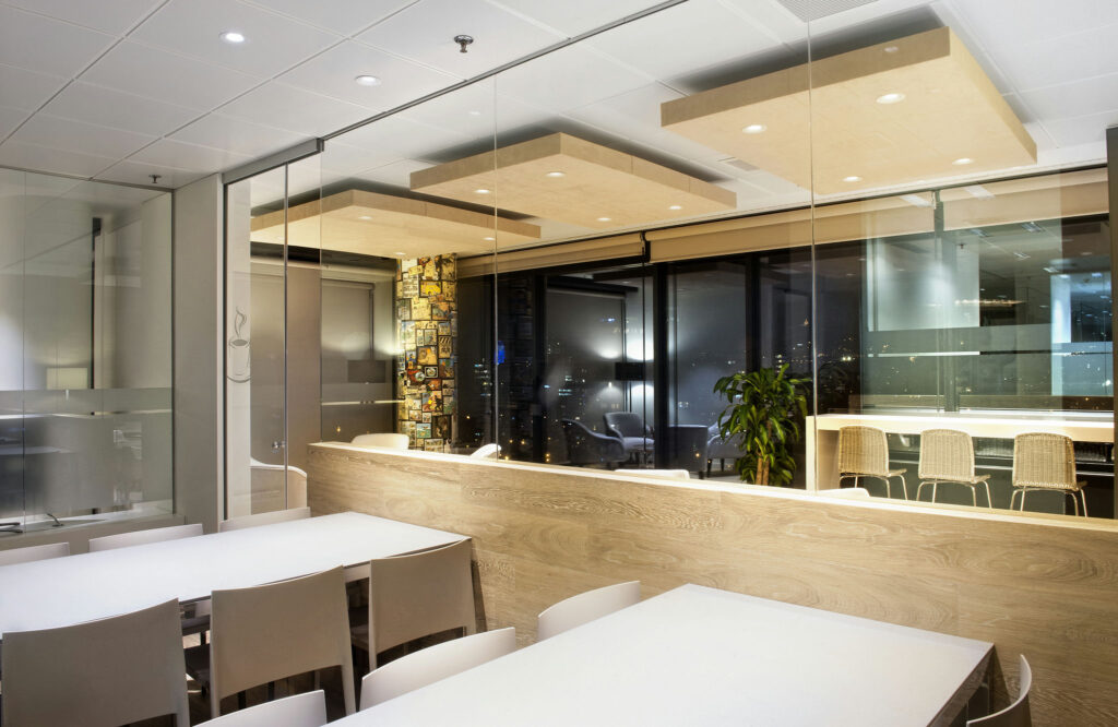 Espacio de Oficina Moderna con Vistas del Skyline de la Ciudad Un interior de oficina contemporáneo con paredes de cristal, una gran mesa blanca, sillas minimalistas y un mostrador de madera con taburetes de bar elegantes, iluminado por una suave iluminación. El fondo muestra obras de arte coloridas y grandes ventanas que ofrecen una vista panorámica del skyline de la ciudad por la noche.