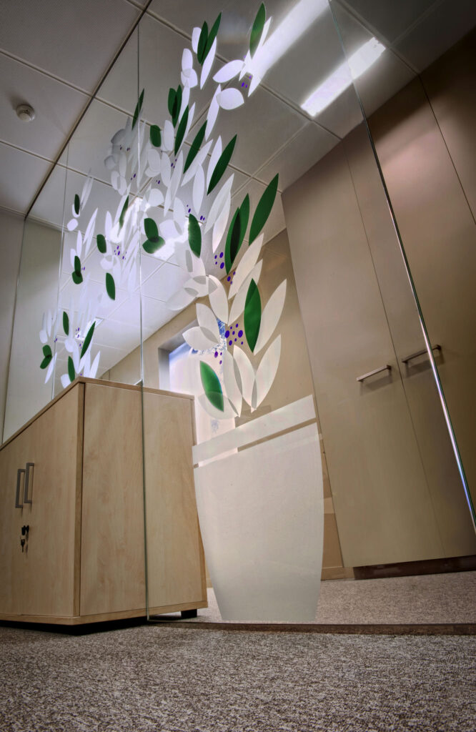 Recepción de oficina moderna con diseño elegante de madera y vidrio Una recepción de oficina contemporánea que presenta un escritorio de madera, una partición de vidrio con motivos decorativos de hojas, y un ambiente brillante y acogedor con iluminación empotrada y una alfombra texturizada.