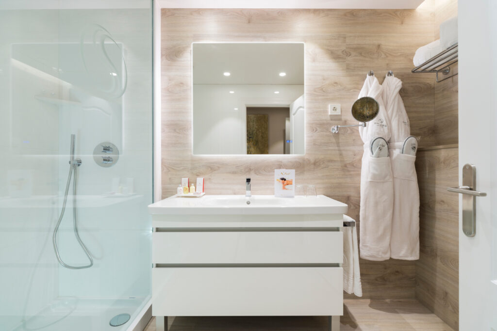 Baño moderno con estilo minimalista en madera clara Baño elegante con diseño minimalista, destacando una encimera blanca y paredes de madera clara, con un espejo cuadrado y productos de cuidado personal.