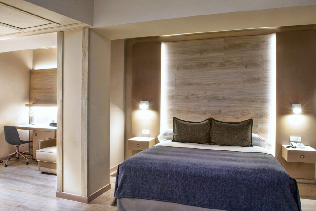 diseño de dormitorio moderno con elegancia sutil un dormitorio moderno con pared de acento de madera, iluminación ambiental, cama acolchada con dos cojines decorativos y muebles minimalistas, incluyendo un pequeño escritorio con silla y colores cálidos en las paredes