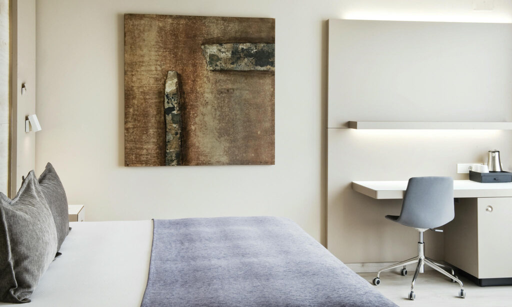 Dormitorio moderno minimalista con elegancia serena Dormitorio contemporáneo minimalista con cama gris claro, paredes claras, y elementos en madera, complementado por un arte abstracto en tonos terrosos.