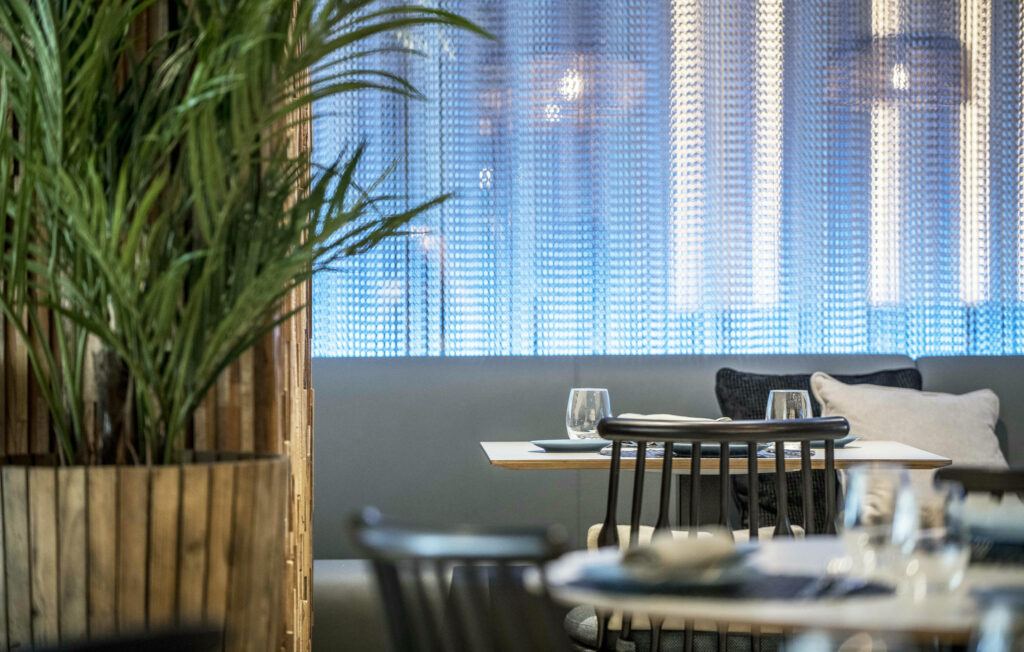 Diseño de interior de restaurante contemporáneo con elegancia minimalista Interior moderno de un restaurante contemporáneo que presenta mesas elegantes, sillas negras y una iluminación azul suave, complementado con una planta decorativa.