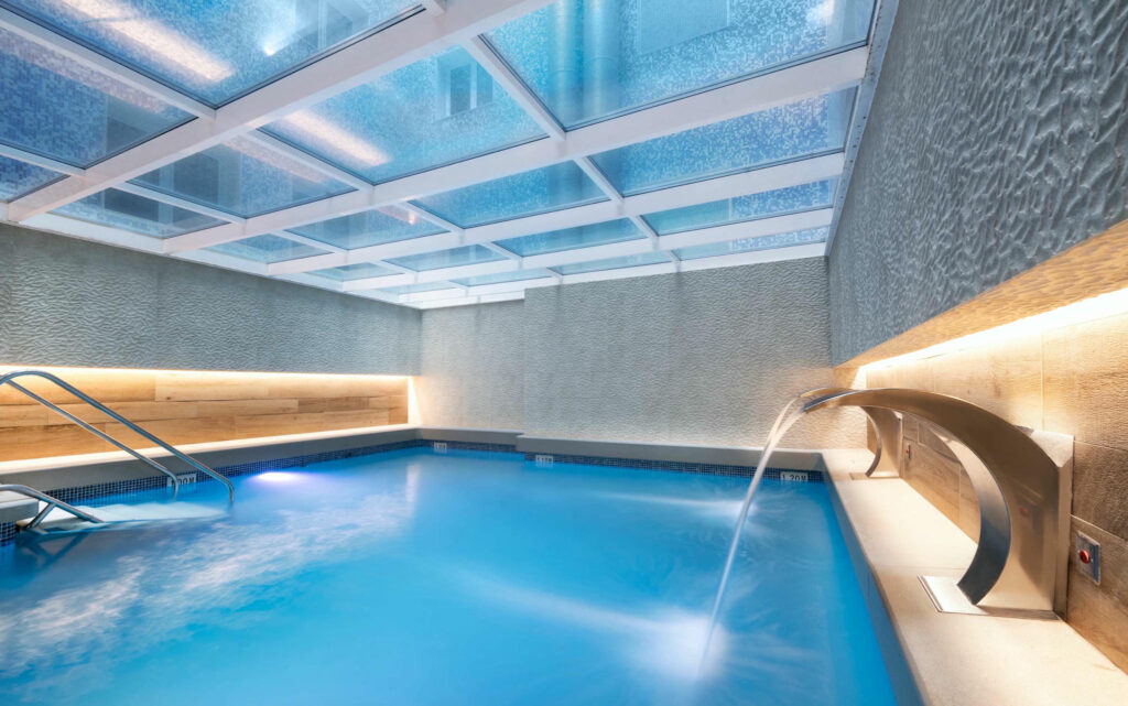 Piscina interior moderna Piscina elegante con luz natural y acabados en mármol.