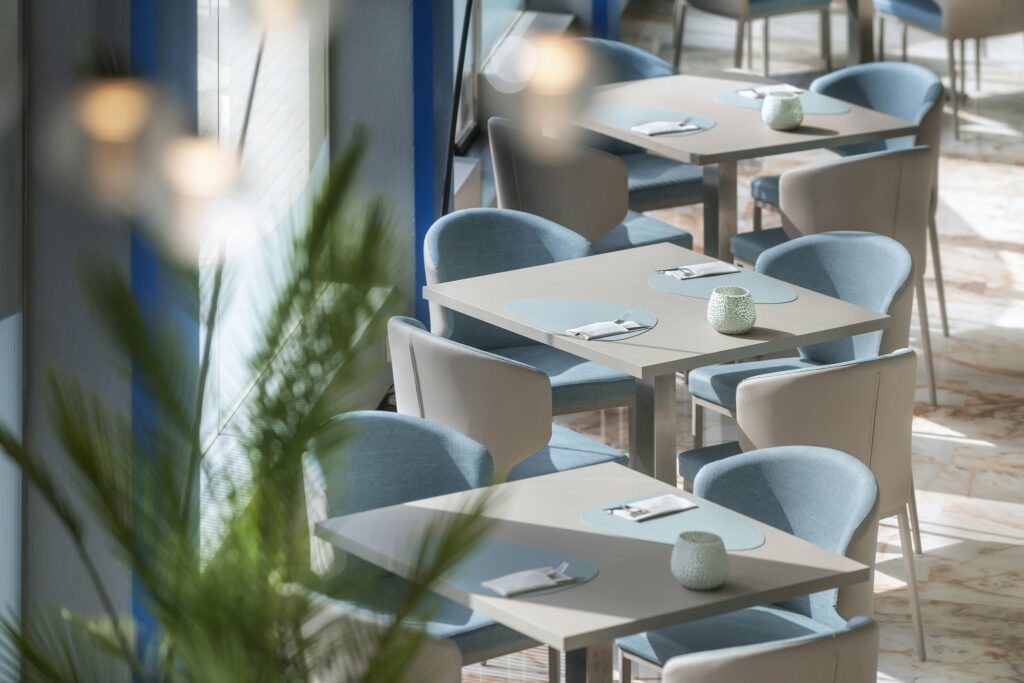 Diseño contemporáneo de un restaurante elegante con materiales naturales Interior de un restaurante moderno con mesas de madera clara, sillas tapizadas en azul y decoración minimalista que integra elementos naturales.