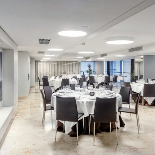 Comedor moderno con mesas blancas y sillas oscuras.