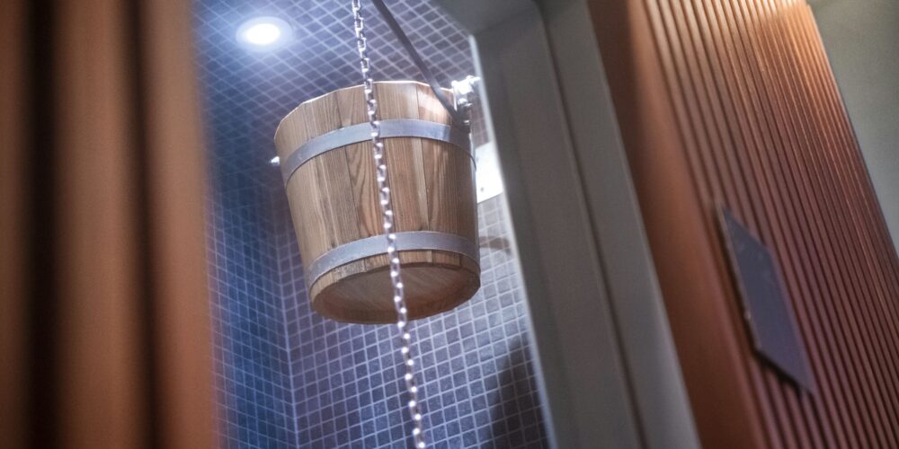 Un cubo de madera colgado de una cadena en un baño elegante con azulejos azules y una iluminación brillante, creando una atmósfera relajante.