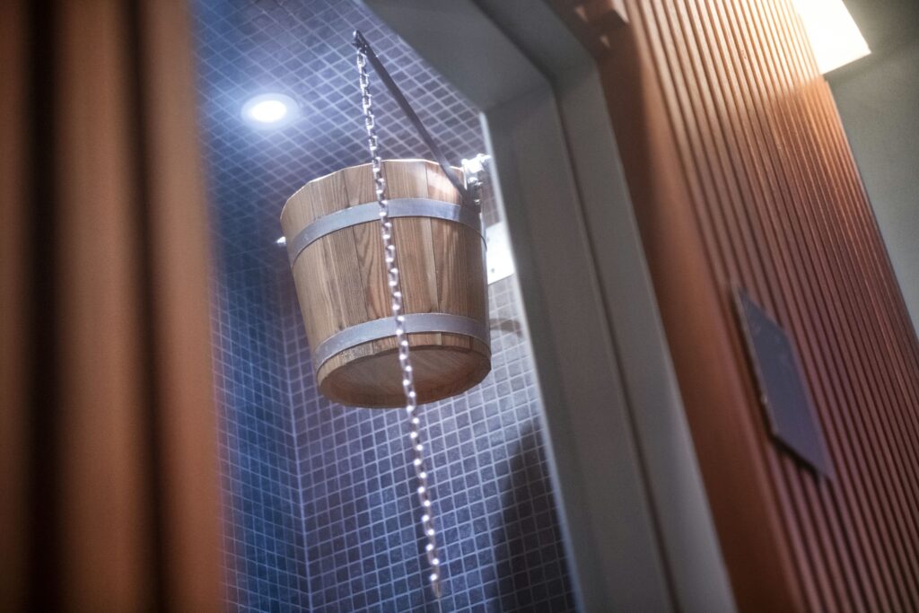 Cubo de Madera Suspendido en Baño Moderno con Azulejos Un cubo de madera colgado de una cadena en un baño elegante con azulejos azules y una iluminación brillante, creando una atmósfera relajante.