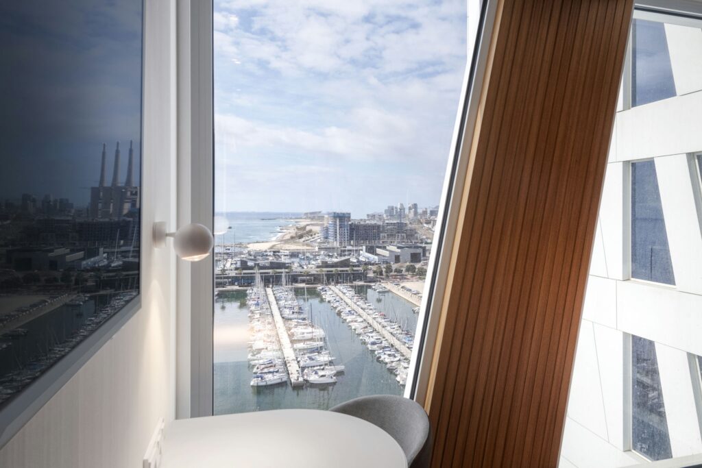 Interior Moderno Elegante con Vista al Puerto Espacio de vida moderno con una gran ventana que muestra una vista escénica del puerto, con barcos, el horizonte de la ciudad, acentos de pared de madera y elementos de diseño contemporáneo.