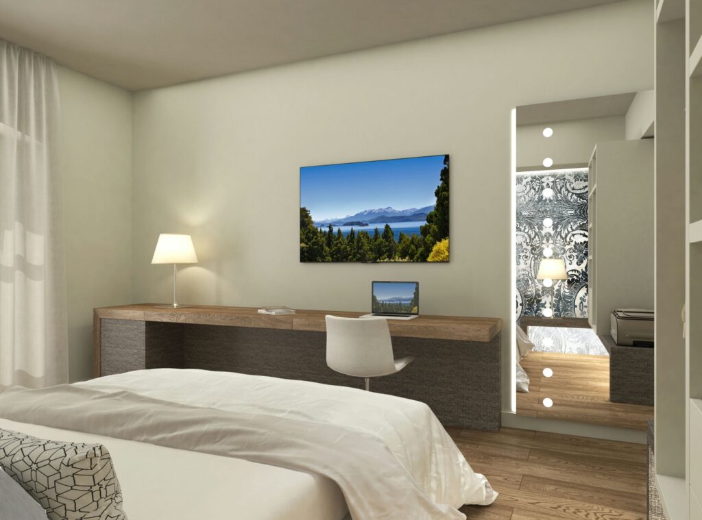 Diseño de interiores de dormitorio moderno en Barcelona con elementos arquitectónicos elegantes Interior de un dormitorio moderno en Barcelona, destacando una cama con sábanas blancas, un escritorio de madera y una gran televisión. El espacio está iluminado por luz natural y cuenta con un espejo de cuerpo entero con iluminación integrada.