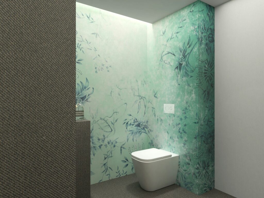 Diseño de Baño Moderno en Barcelona con Papel Tapiz Floral Proyectos de diseño de interiores en Barcelona: baño moderno con papel tapiz verde claro y patrones florales, inodoro blanco y suelo gris texturizado, destacando funcionalidad y estética contemporánea.
