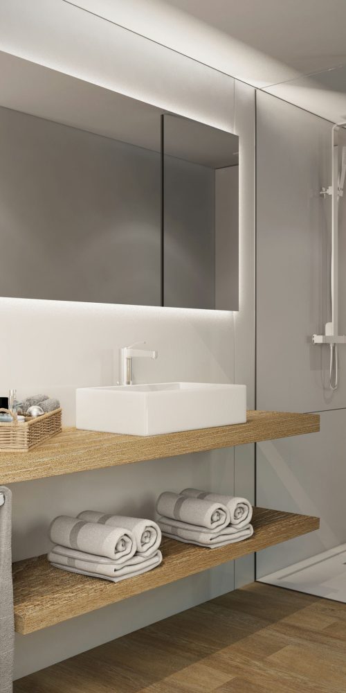 Interior de baño moderno y elegante con diseño minimalista, que presenta una encimera de madera, lavabo cuadrado blanco y toallas grises organizadas. La iluminación natural resalta los materiales de cristal y madera en un ambiente contemporáneo típico de la arquitectura de alta gama en Barcelona.