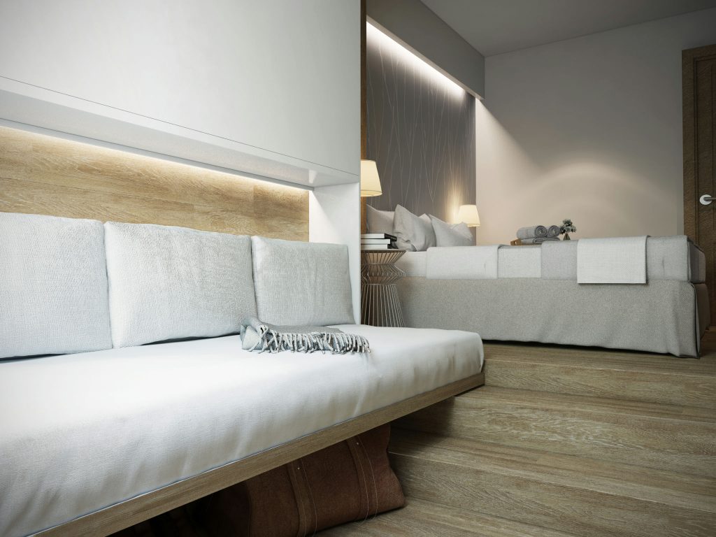 Habitación moderna y lujosa en Barcelona: diseño de interiores sofisticado Un dormitorio moderno en Barcelona con un diseño de interiores contemporáneo, que presenta una estética minimalista en tonos blancos, beige y madera natural. Incluye un sofá cómodo en primer plano, una cama bien hecha y detalles arquitectónicos elegantes.