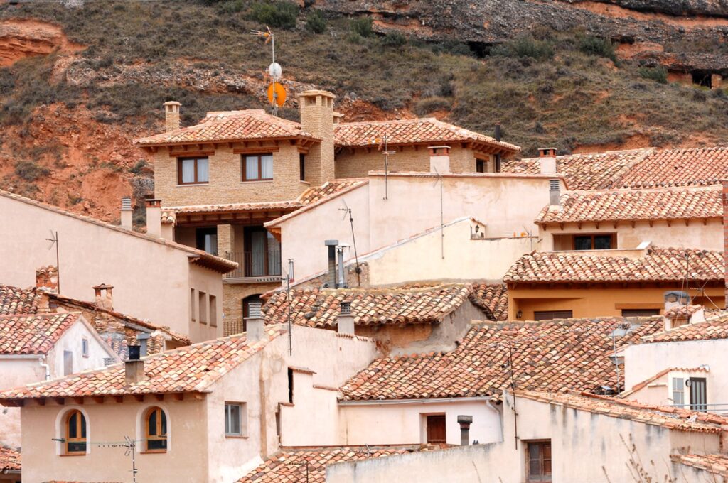 Casa en Molinos: Una vista panorámica que muestra un pintoresco pueblo aragonés con una mezcla de arquitectura tradicional y moderna, con tejados de terracota, edificios beige y blancos situados contra un fondo montañoso.