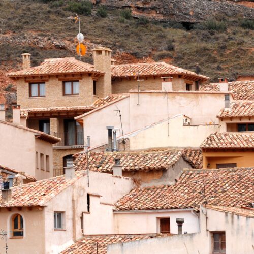 Casa en Molinos: Una vista panorámica que muestra un pintoresco pueblo aragonés con una mezcla de arquitectura tradicional y moderna, con tejados de terracota, edificios beige y blancos situados contra un fondo montañoso.