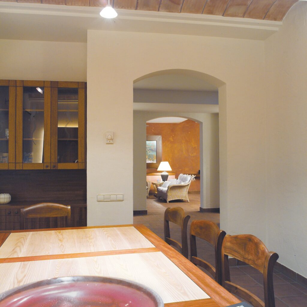 Comedor Moderno con Toque Rústico en un Hogar Acogedor Vista interior de un comedor moderno que presenta una mesa de madera clara y sillas de madera oscura, que da a una sala de estar iluminada cálidamente con asientos acogedores y una lámpara, mostrando una mezcla de diseño contemporáneo y rústico.