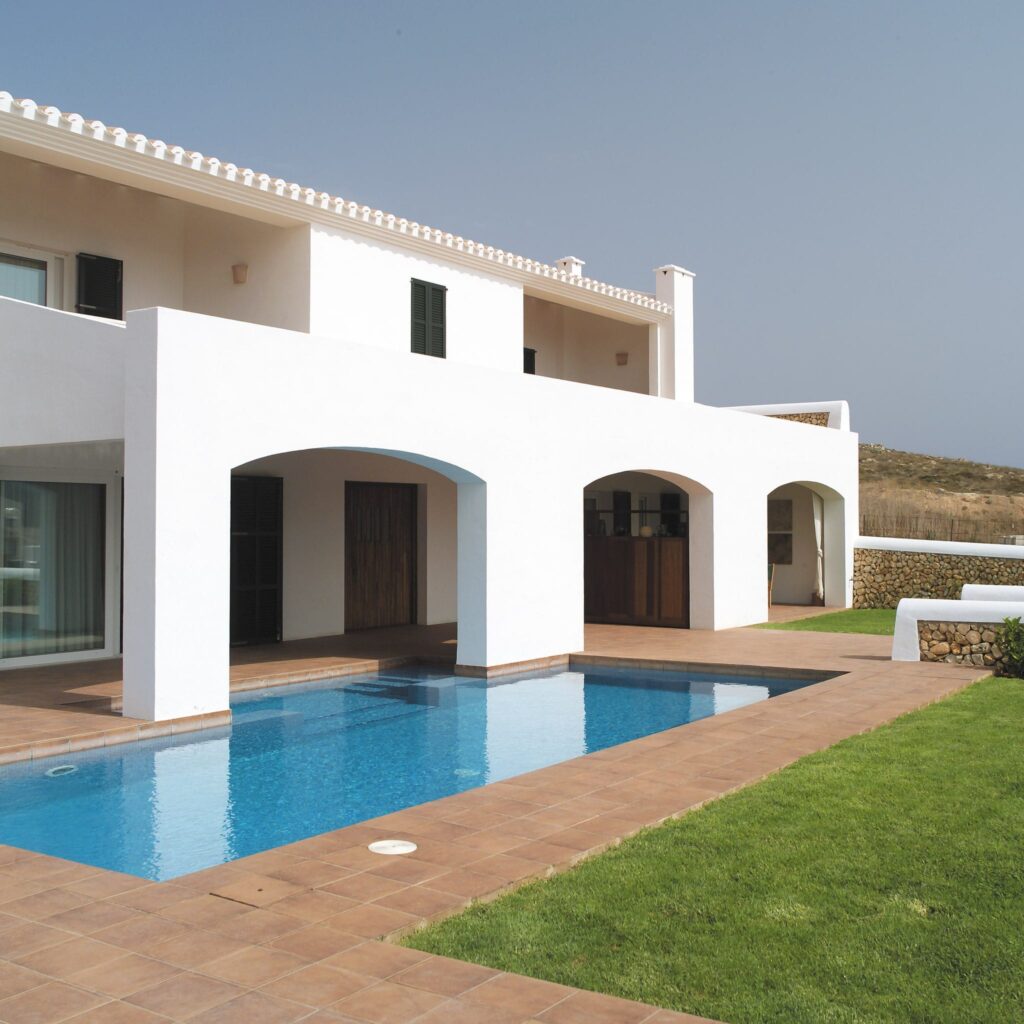 Moderna Villa de Dos Pisos con Piscina y Diseño Minimalista Una elegante villa moderna de dos pisos con exterior blanco, aberturas en arco y una piscina rectangular rodeada de un césped bien cuidado, situada en una suave colina.