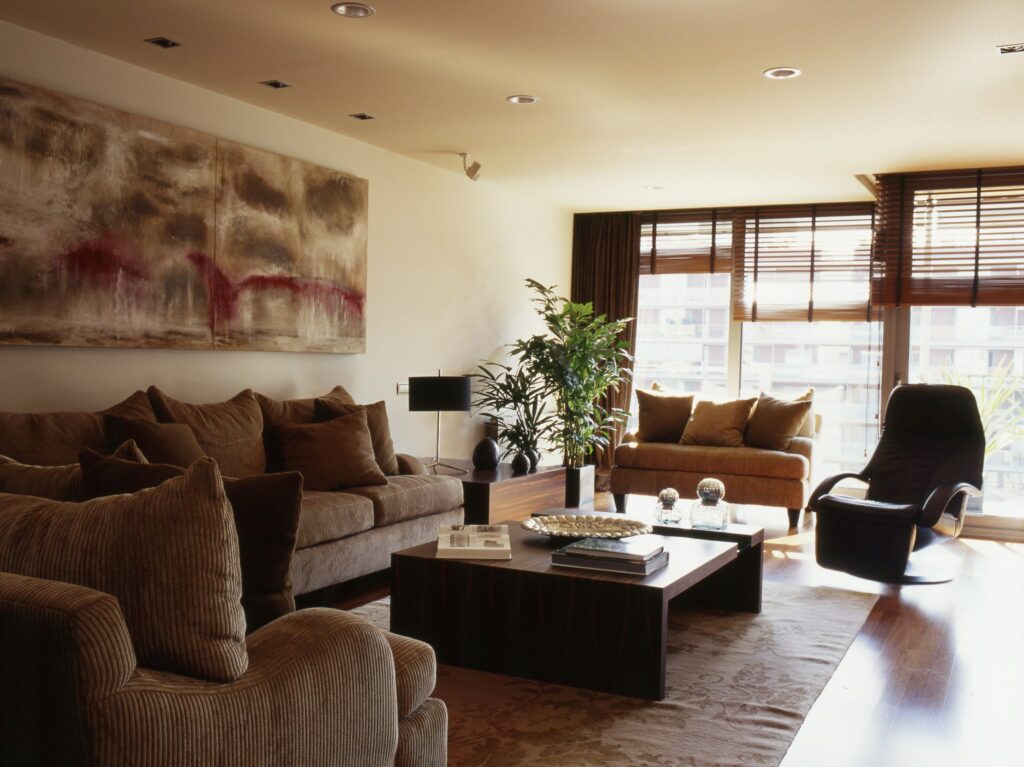 Piso en Calle Can Rabia: Una sala de estar moderna que muestra dos sofás acolchados con cojines alrededor de una mesa de café contemporánea, con una planta decorativa y grandes ventanales con persianas de madera que permiten que la luz natural llene el espacio. Las paredes exhiben arte abstracto, creando una atmósfera sofisticada en un entorno de suelo elegante.