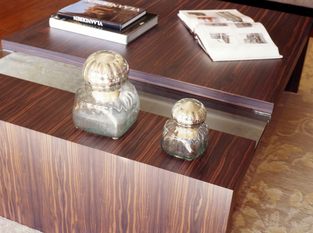 Mesa de café moderna y elegante con acentos decorativos Una mesa de café estilosa con un acabado de madera oscura rica, coronada con dos tarros de vidrio decorativos con tapas metálicas, y una pila de libros parcialmente visibles sobre una suave alfombra de color claro.
