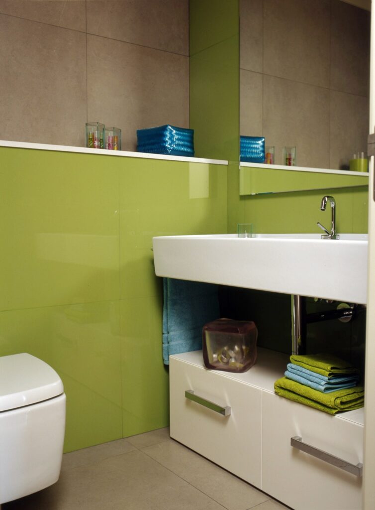 Baño Moderno con Paredes Verdes Vibrantes y Decoración Elegante Vista interior de un baño moderno con paredes verdes vibrantes, un elegante lavabo blanco sobre un mueble bajo con cajones extraíbles, un inodoro contemporáneo y toallas coloridas en azul y verde organizadas ordenadamente.