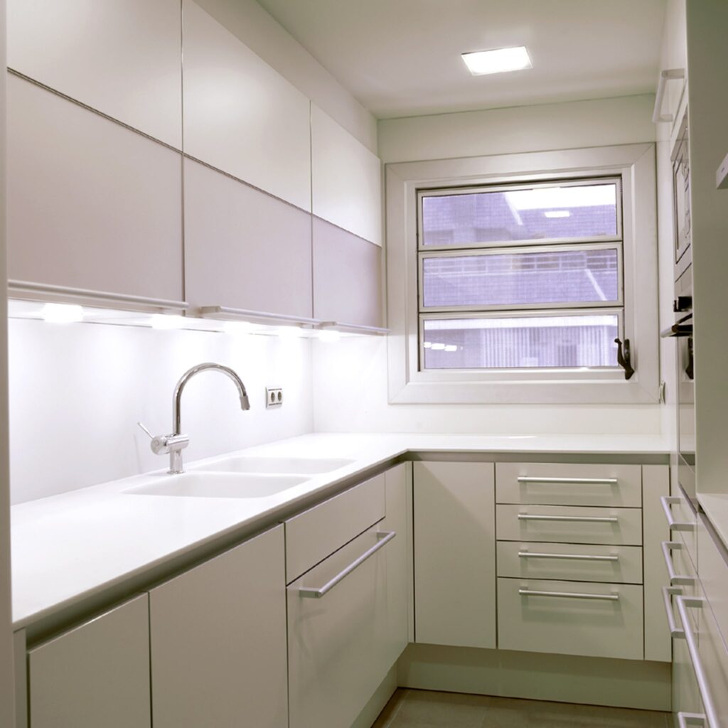 Cocina Moderna y Contemporánea en Barcelona - Diseño de Interiores de Alta Gama Moderna cocina de alta gama en Barcelona, con armarios de acabado brillante en tonos neutros, encimera minimalista y grifo elegante, iluminada por luz natural y LEDs.