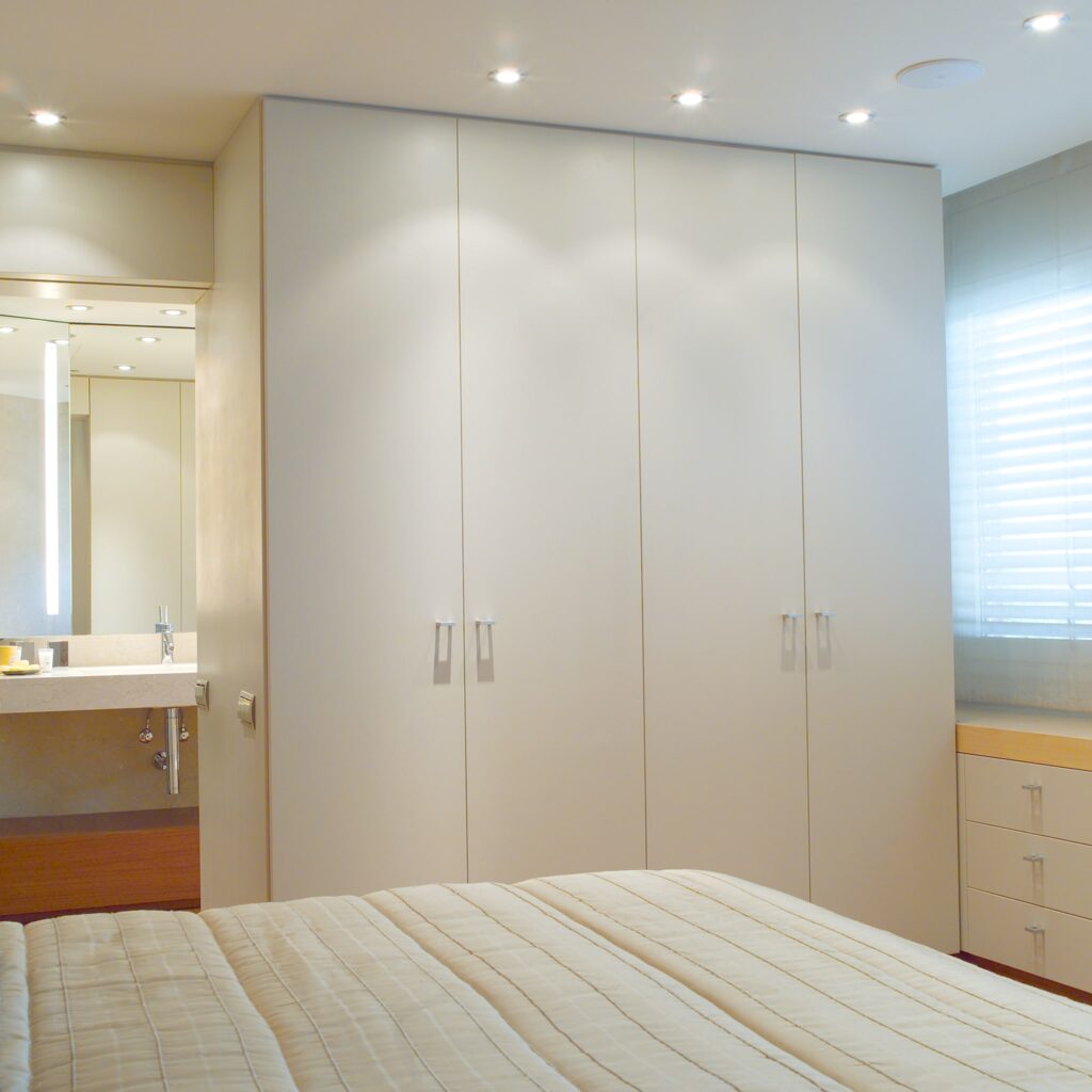 Interior de dormitorio moderno con diseño minimalista Un dormitorio moderno, brillante y espacioso, con paredes de colores claros, una cama bien hecha con una manta acolchada, armarios empotrados elegantes, un tocador contemporáneo con espejo y luz natural filtrándose a través de una ventana.