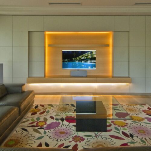Torre en Alella: Salón contemporáneo en Barcelona, con sofá marrón de cuero, mesa de cristal y alfombra floral, destacando la funcionalidad y estética en proyectos de arquitectura de alta gama.