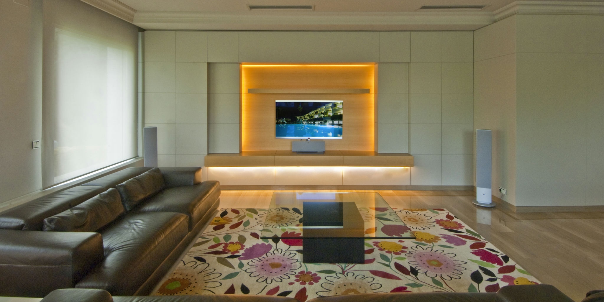 Torre en Alella: Salón contemporáneo en Barcelona, con sofá marrón de cuero, mesa de cristal y alfombra floral, destacando la funcionalidad y estética en proyectos de arquitectura de alta gama.